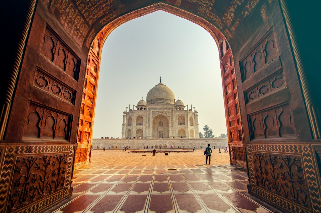 Vista enmarcada del Taj Mahal a través del arco de la puerta principal de arenisca roja, contrastando el mármol blanco del mausoleo con los muros rojizos